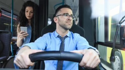 a bus driver looks out the window with a serious look on his face while sitting at the wheel of his vehicle.