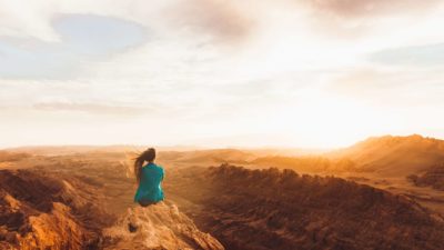 A woman sits looking out at a rocky, arid mountain range at the effects of climate change.