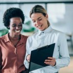 Two female executives looking at a clipboard together.