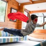Child with superhero mask and cape flies after jumping on sofa