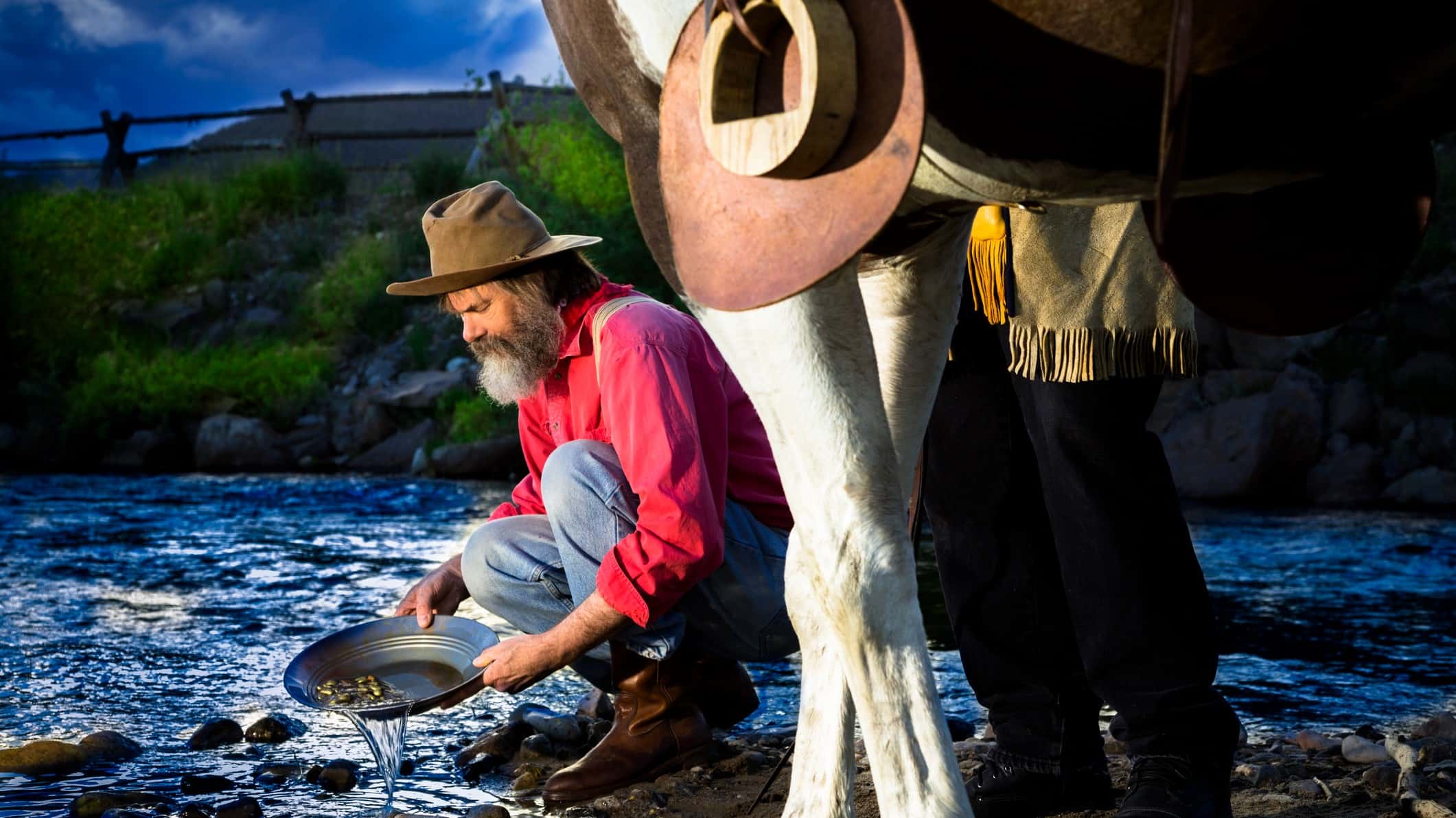 Miner panning for gold next to a horse in the outdoors.