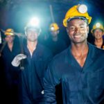 Miner team in the caves with their lights on and smiling