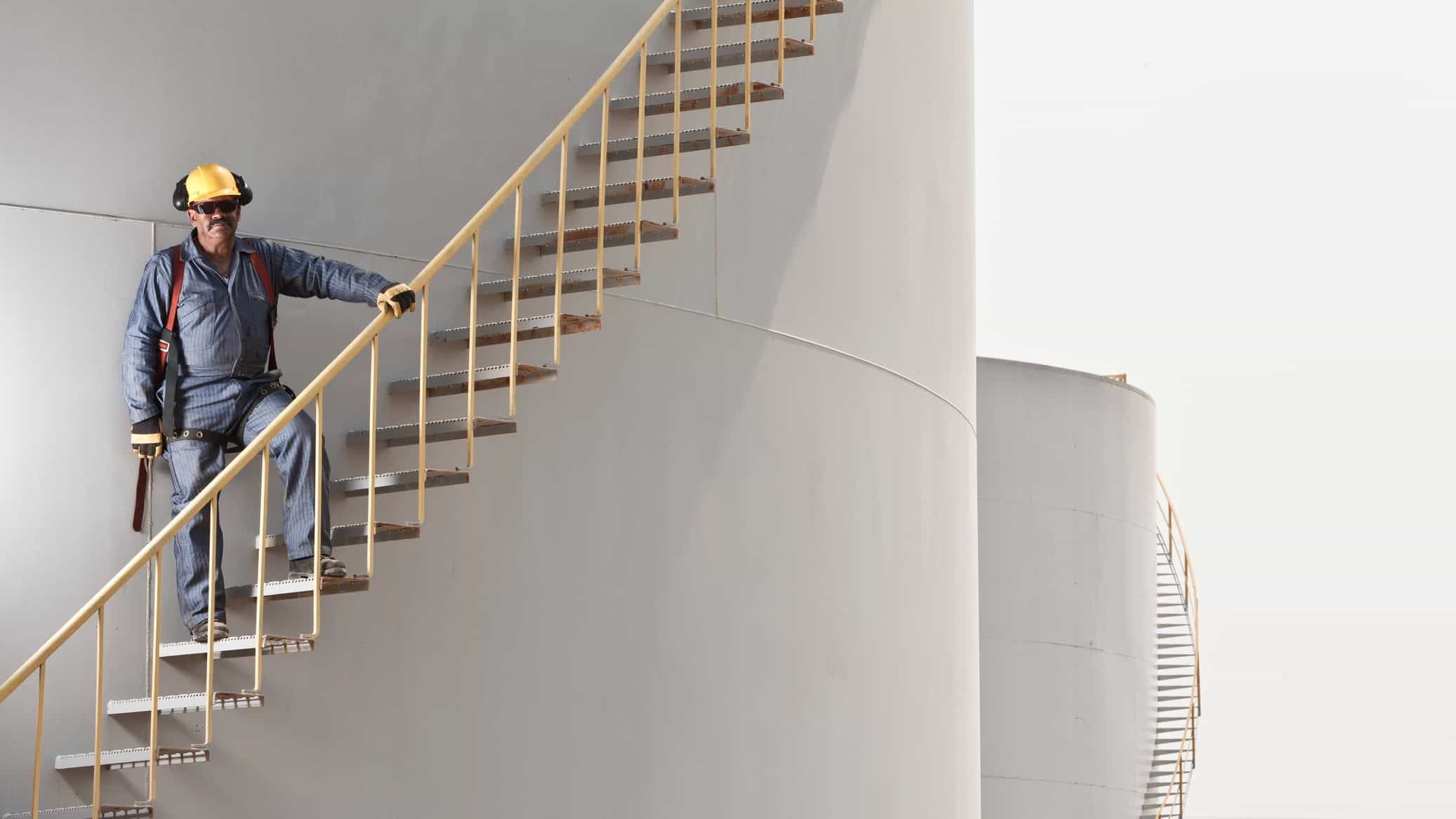 A plant worker walks up stairs on the outside of an oil silo.