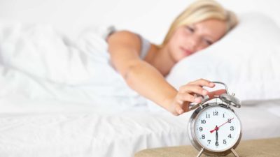 Woman in bed rolls over to hit clock