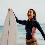 woman on the beach in her swimmers holding her surfboard