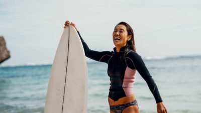 woman on the beach in her swimmers holding her surfboard