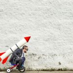 Man with a rocket strapped to his back on a tiny bicycle ready to take off.