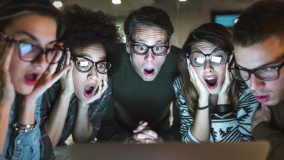 Five workers look shocked around computer screen with mouths open