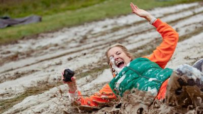 A woman in a green vest has fun sliding down a muddy slope.