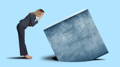 A businesswoman peers at a big square trying to fit into a round hole.