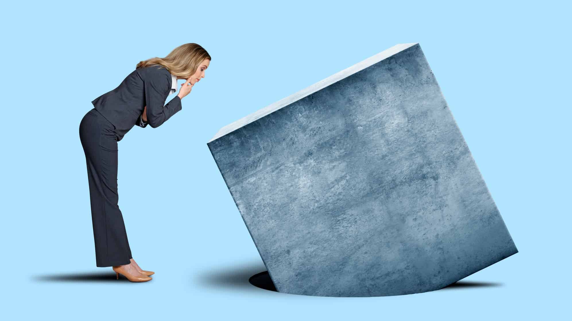 A businesswoman peers at a big square trying to fit into a round hole.