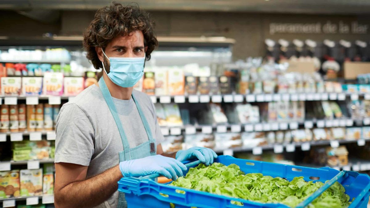 Male supermarket worker stands in front of a crate of fresh lettuce, fulfilling online shopping orders.