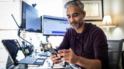 man on his phone in front of all his computer screens checking the market and the ASX 200