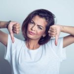 A young woman with tattoos puts both thumbs down and scrunches her face.