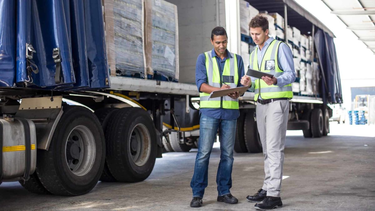 two men look at delivery manifest of loaded truck