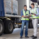 two men look at delivery manifest of loaded truck