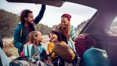 family taking gear out of back of car for camping