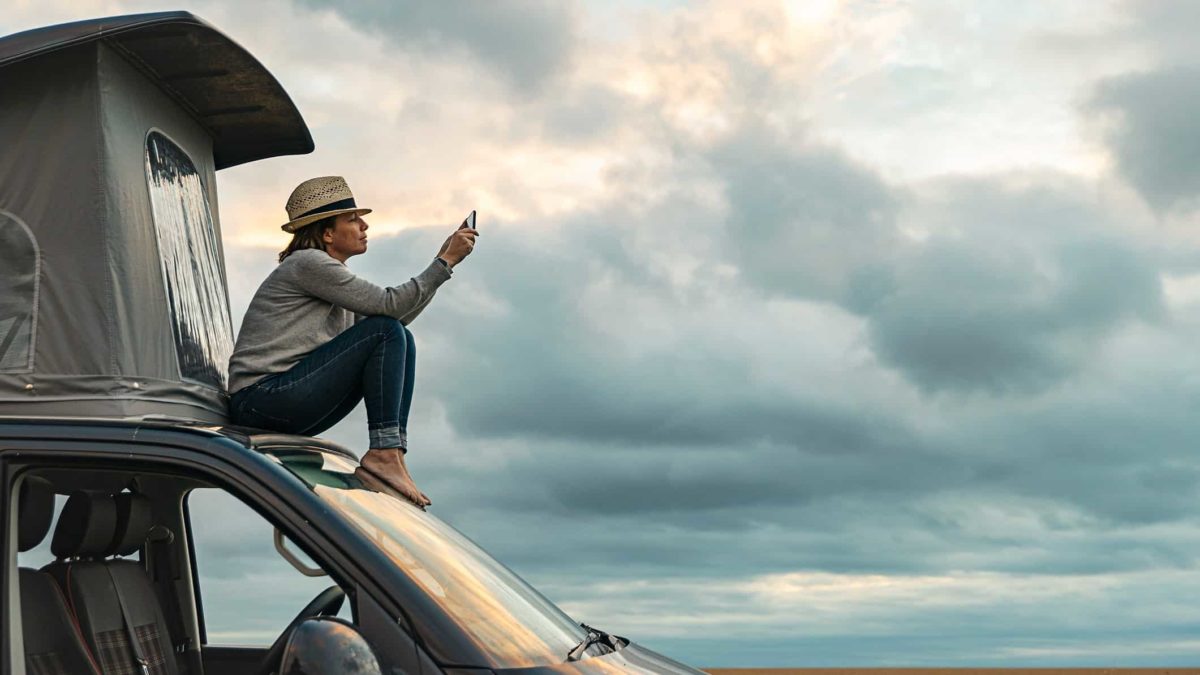 man sits on top of truck taking a photo of the sky