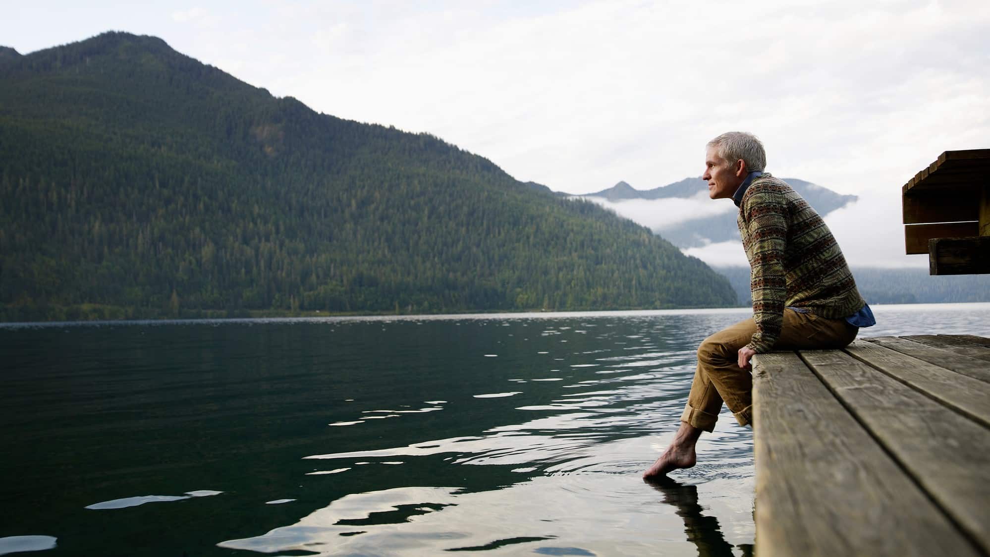 man sits on the dock enjoying the quite of the lake in the mountains