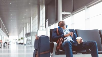 A trendy man sinks down in an airport terminal chair, waiting.