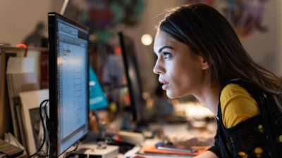 A woman stares at a computer with her face just inches from the screen.