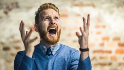 A smartly-dressed man screams to the sky in a trendy office.