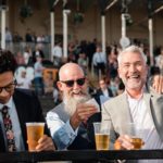 Two men celebrate while another holds his head in his hands, after watching the race.