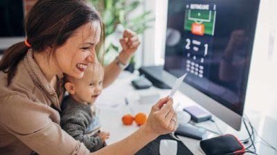 A woman sits at her home computer with baby on her lap, and the winning ticket in her hand.