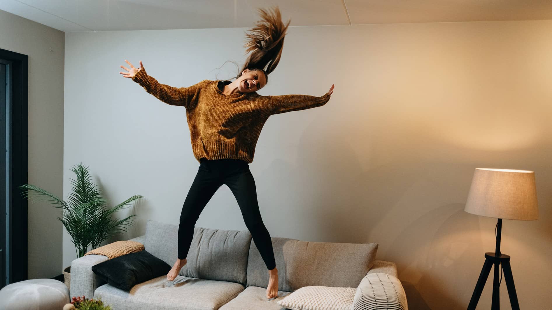 A woman leaping for joy on her couch, happy to be a home owner.