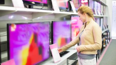 Woman looking at prices for televisions in electronics store representing increasing sales yet adecline in the JB Hi-Fi share price over FY22