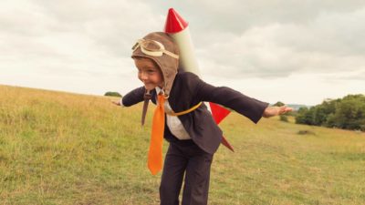 Boy dressed in business suit with rocket strapped to back ready to take off