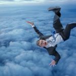 Man in business suit above the clouds plummeting downwards back first