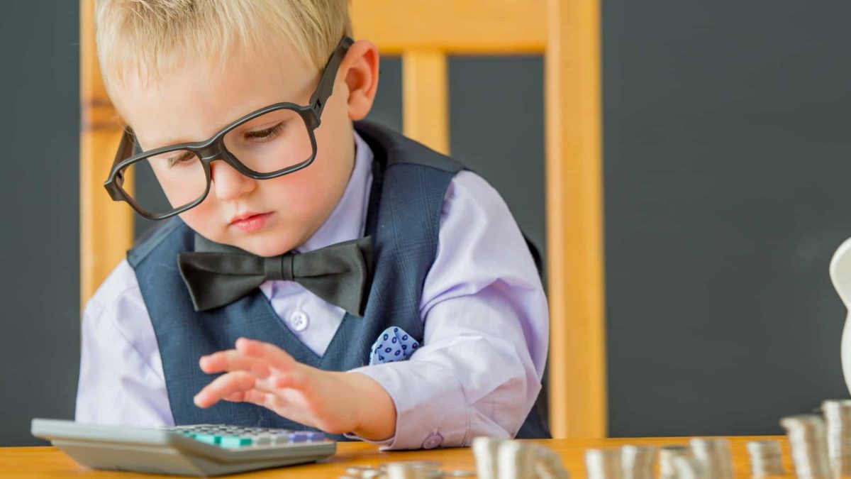 Young boy wearing suit and glasses counts his money using a calculator.