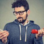 A man in a sweatshirt holds two different phones to compare telco services.