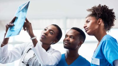 Three healthcare workers look and point at at medical image