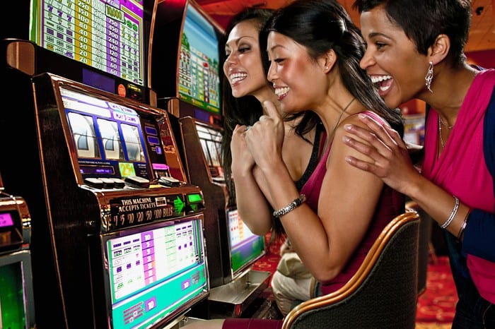 Three women laughing and enjoying their gambling winnings while sitting at a poker machine