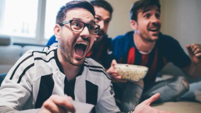 Man holding up betting slip and cheering along with two friends in front of TV