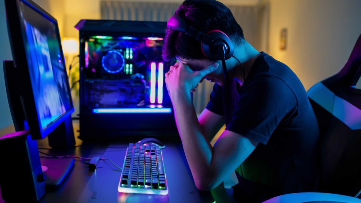 A gamer slumps his head in his hands in front of two gaming screens