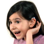 Young girl shows hearing aid while smiling