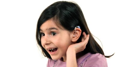 Young girl shows hearing aid while smiling