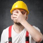 Upset man in hard hat puts hand over face.