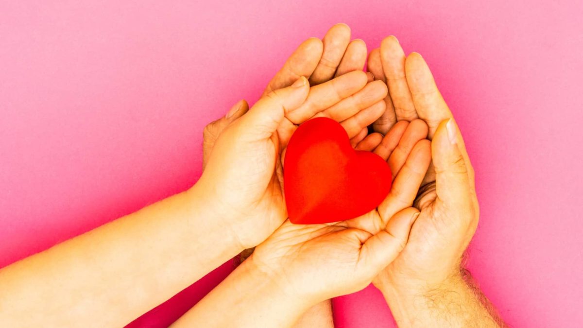 two pairs of hands hold a red heart shape in memory of a loved one