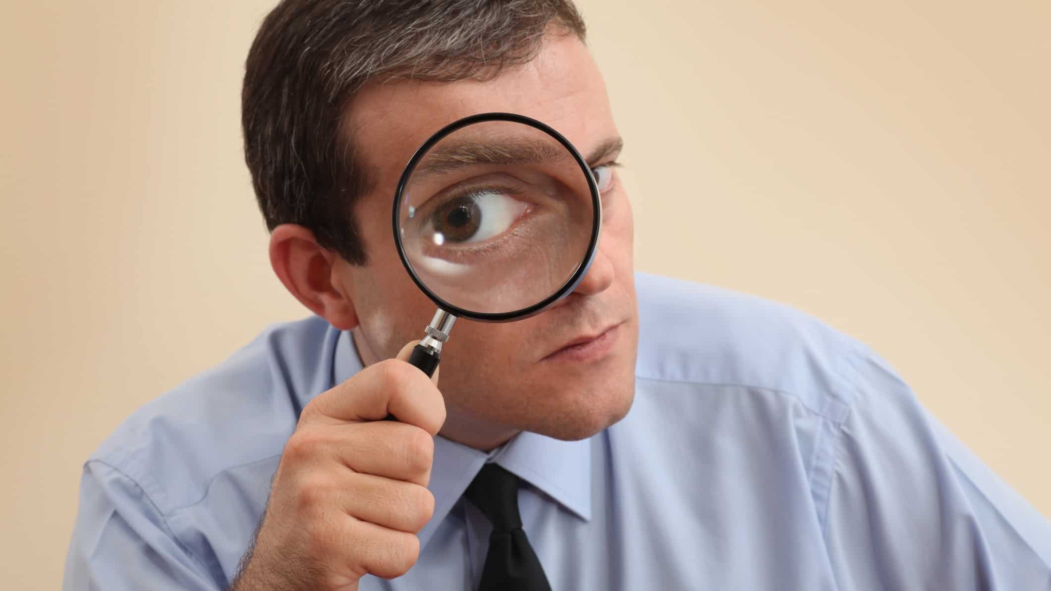 Businessman looks with one eye through magnifying glass