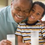 Older man and young boy smiling while drinking milk with milk moustaches