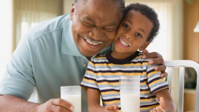 Older man and young boy smiling while drinking milk with milk moustaches