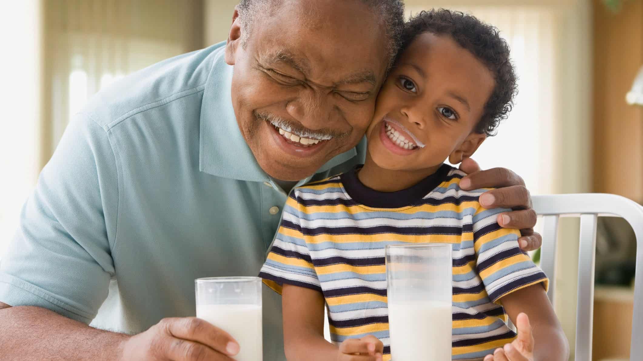 Older man and young boy smiling while drinking milk with milk moustaches