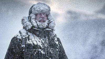 Man covered in snow wearing big thick coat