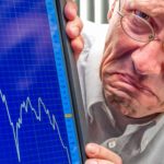 man grimaces next to falling stock graph