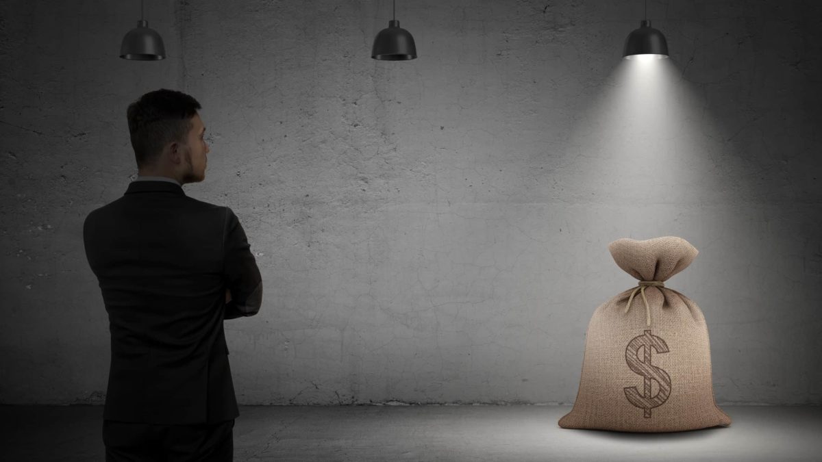 Man in suit looks at bag of money with dollar sign in spotlight