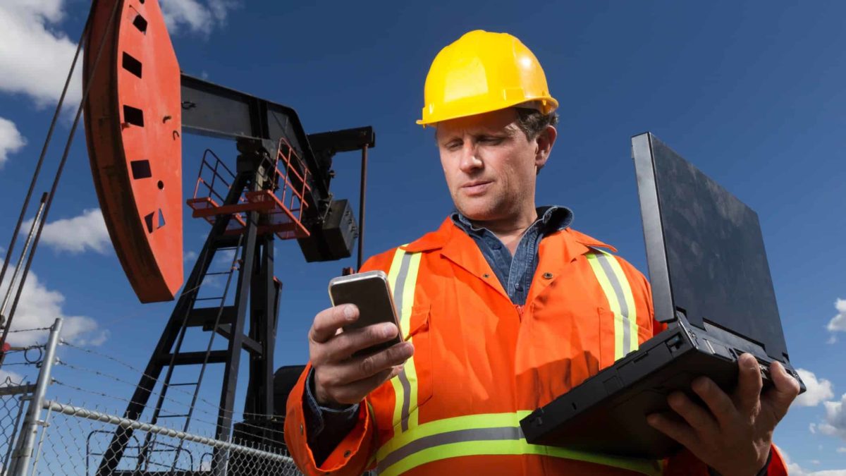 Oil miner holding a laptop and mobile phone looks at his phone and sees the falling oil price and falling Woodside share price